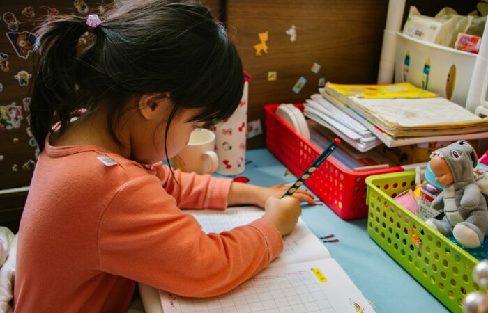 girl in pink long sleeve shirt writing on white paper